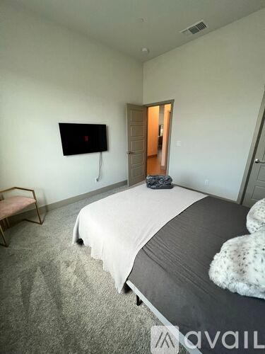 A bedroom with a bed, a chair, and a TV mounted on the wall.