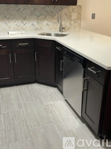 A kitchen with a white counter top and dark brown cabinets.