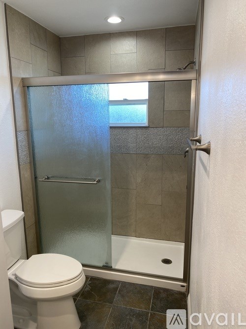 A bathroom with a toilet, a glass shower door, and a tiled floor.