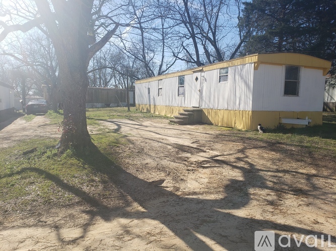 A white and yellow trailer is parked in a grassy area with a tree in the foreground.