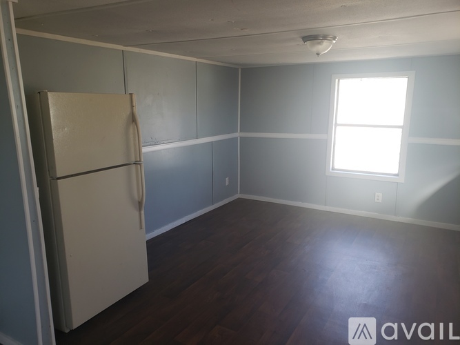 A room with a white fridge and wooden floor.