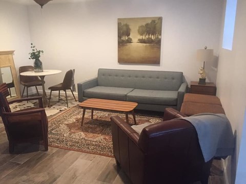 A living room with a grey couch, a wooden coffee table, a round table with chairs, and a painting on the wall.
