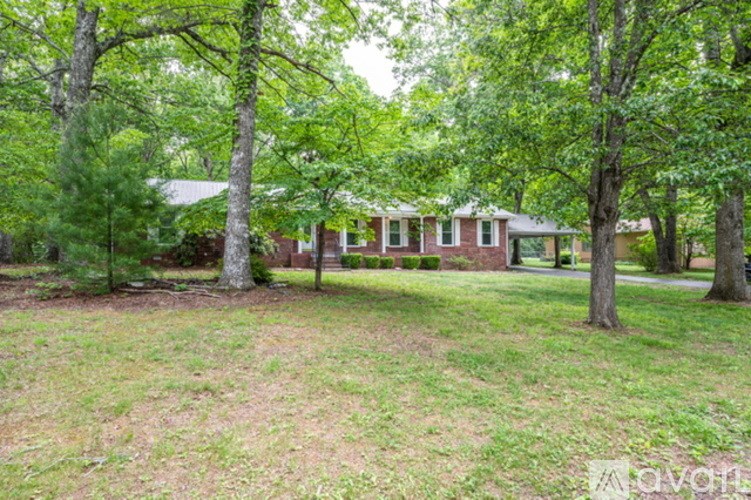 A house is surrounded by trees in a grassy area.