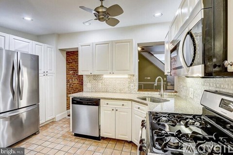 A modern kitchen with a stainless steel refrigerator, a black stove top, and white cabinets.