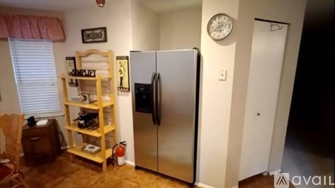 A kitchen with a refrigerator, a clock, and a shelf with a microwave on it.