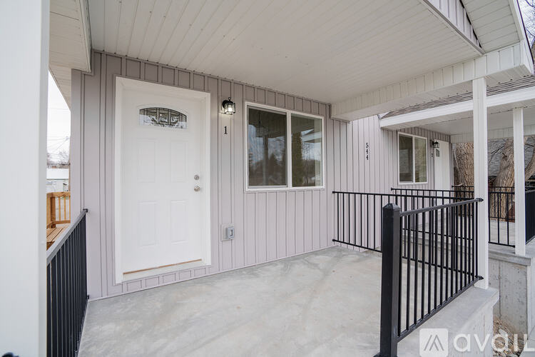 A white door is on the left side of a house with a black railing.