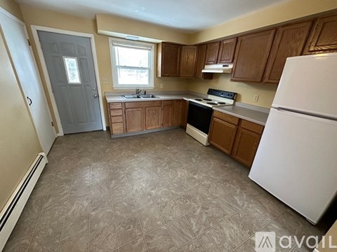 A kitchen with a white refrigerator, wooden cabinets, and a tile floor.