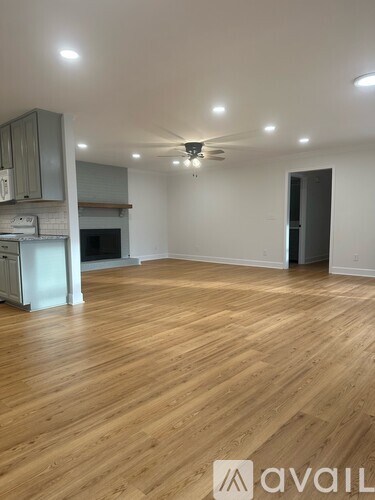 A spacious room with wooden flooring and a kitchen area with a refrigerator, oven, and microwave.