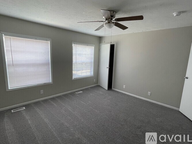 A room with a ceiling fan and two windows.