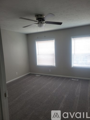 A room with a ceiling fan and two windows.