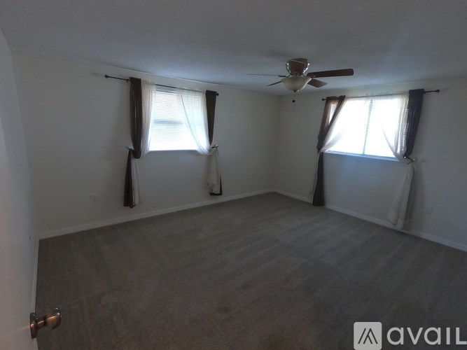 A room with a ceiling fan and two windows with curtains.