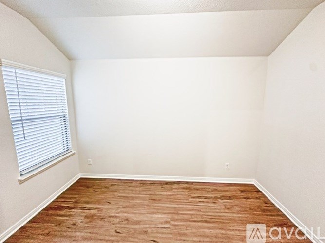 A room with wooden flooring and a window with blinds.