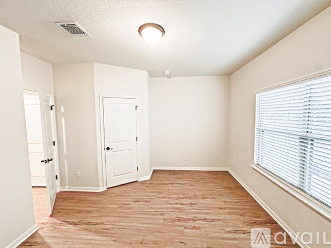 A room with wood flooring and a window with blinds.