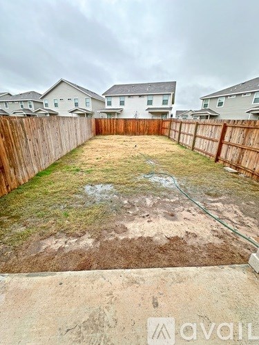 A backyard with a wooden fence and a sandy area in the middle.