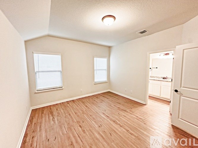 A room with wooden flooring and two windows.