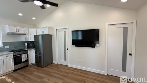 A modern kitchen with a stainless steel refrigerator and a flat screen TV mounted on the wall.