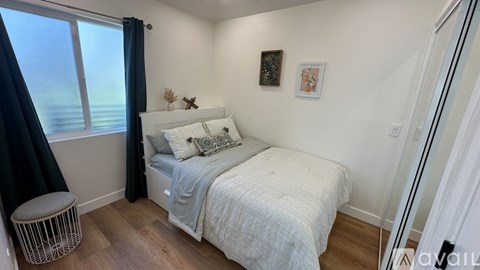 A bedroom with a bed, a window with a view, and a small stool.