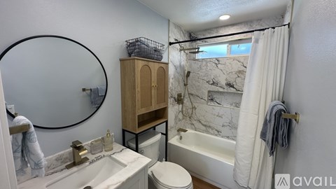 A bathroom with a marble patterned tub, a toilet, a sink, and a wooden cabinet.