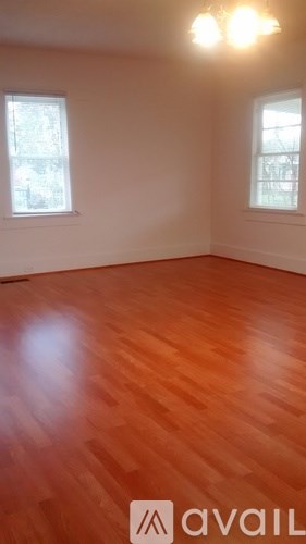 A room with wooden flooring and two windows.