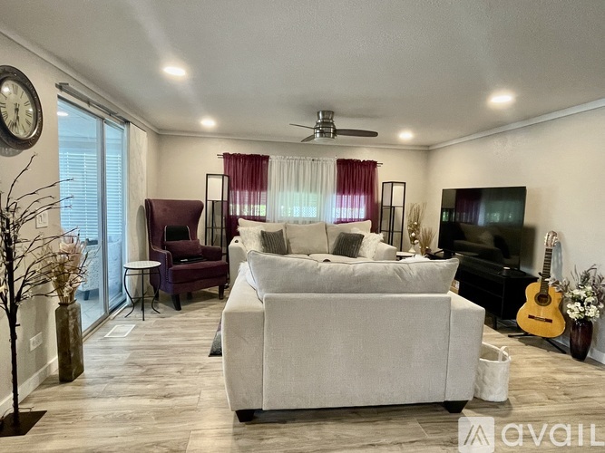 A living room with a white couch, a guitar, and a ceiling fan.