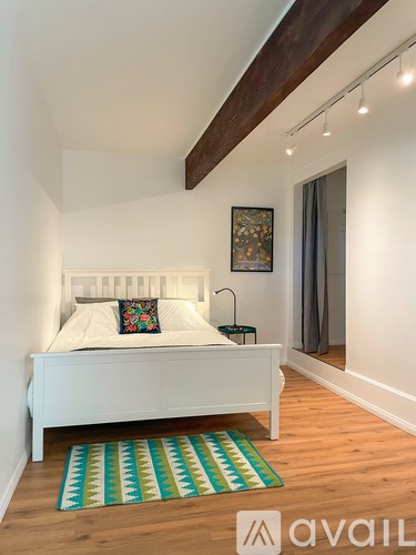 A bedroom with a white bed and a colorful rug.