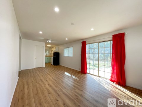 A spacious room with wooden floors and a large window with red curtains.