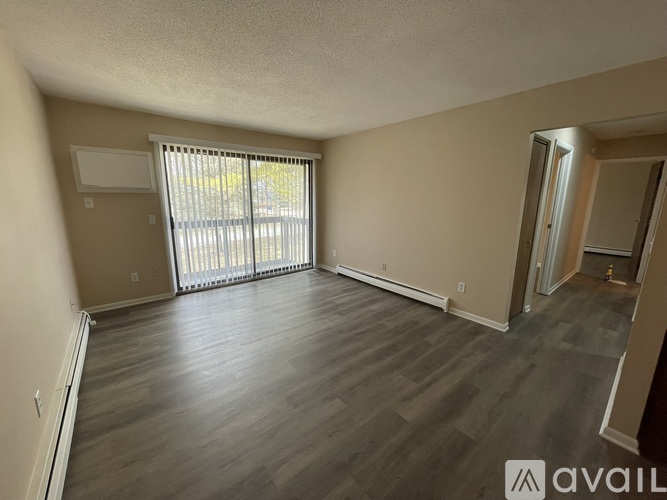 A spacious room with wooden flooring and a sliding glass door.