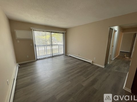 A spacious room with wooden flooring and a sliding glass door.