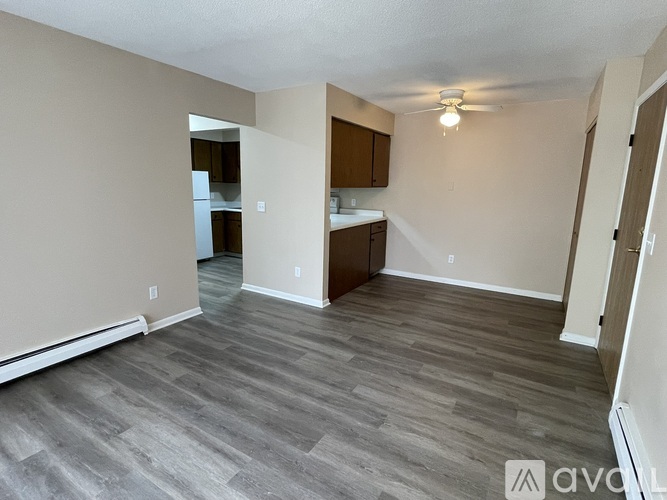 A spacious room with wooden flooring and a kitchen area in the background.