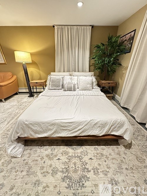 A bedroom with a large bed, a lamp, a chair, and a plant.