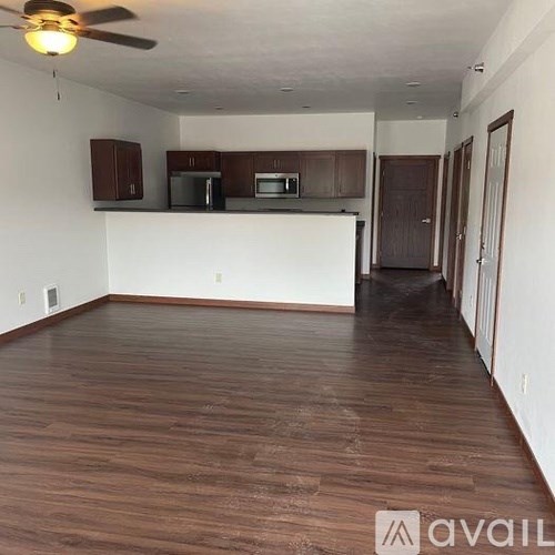 A spacious living room with wooden flooring and a kitchen area in the background.