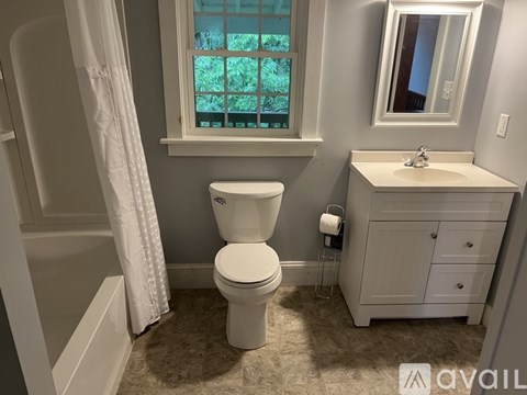 A white toilet sits in a bathroom next to a sink and a window.
