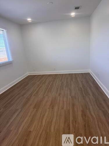 A room with wooden flooring and a window on the left side.
