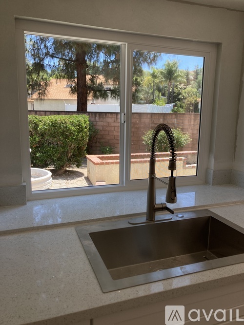 A kitchen sink with a faucet and a window overlooking a backyard.