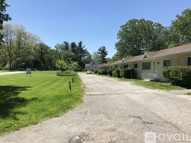 A gravel road leads to a white house with a green lawn on either side.
