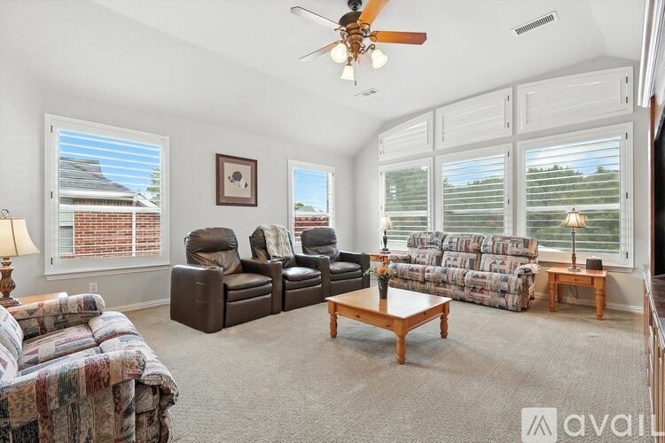 A living room with a brown couch, a chair, a table, and a ceiling fan.
