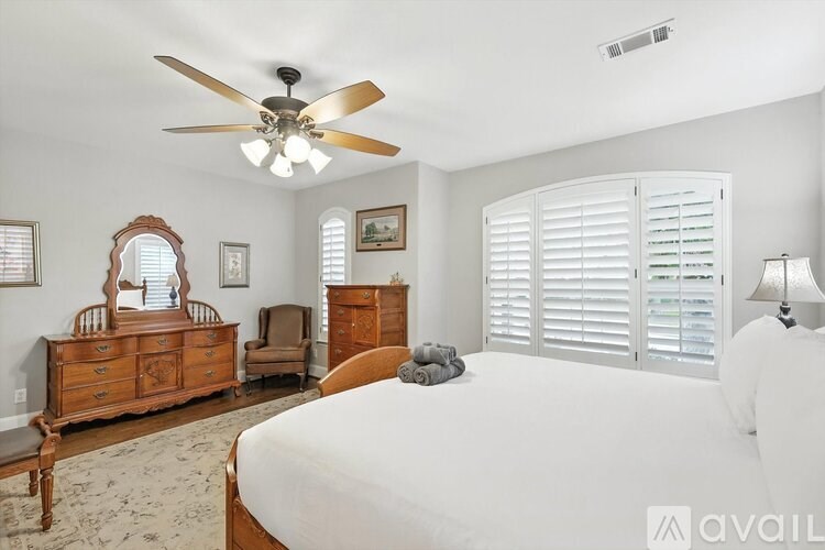 A bedroom with a large bed, a dresser, a chair, a mirror, and a ceiling fan.