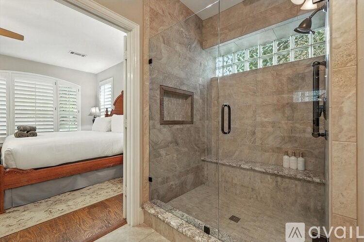 A bathroom with a walk-in shower and a bedroom with a window.
