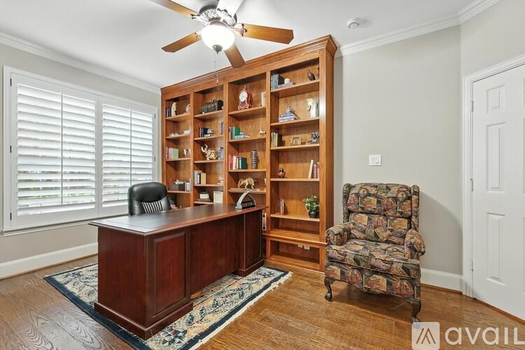 A room with a wooden bookcase, a chair, and a fan.