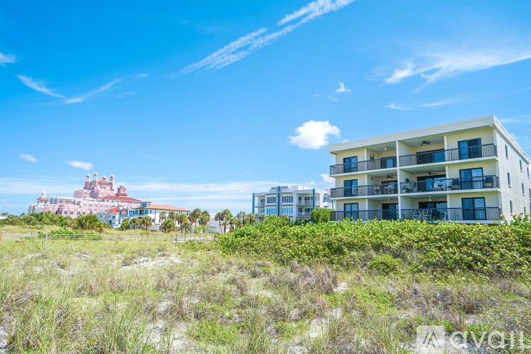 A modern building with balconies is situated on a grassy area with a clear blue sky above.