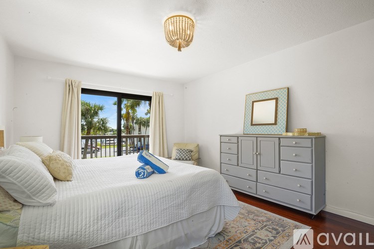 A bedroom with a large bed, a chest of drawers, and a window with a view of a balcony.