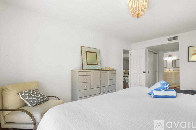 A bedroom with a white bed and a chair with a cushion on it.