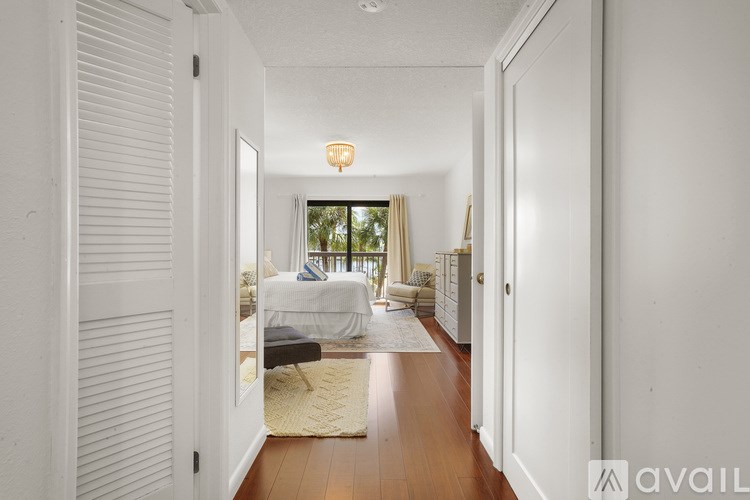 A hallway with white walls and wooden floors leads to a bedroom.