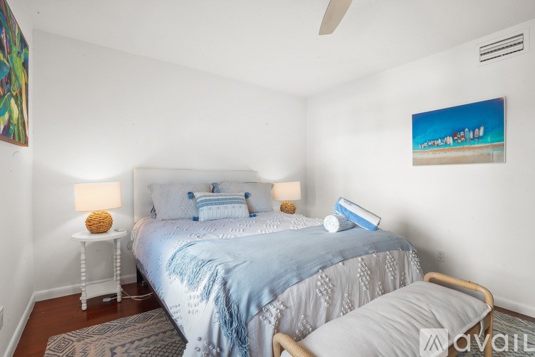 A bedroom with a bed, a nightstand with a lamp, and a painting on the wall.