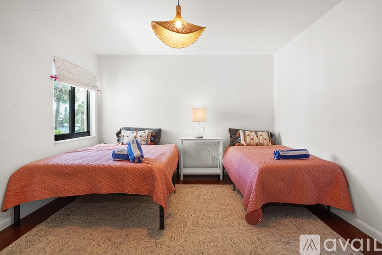 Two twin beds with orange bedspreads in a room with a hanging light fixture.