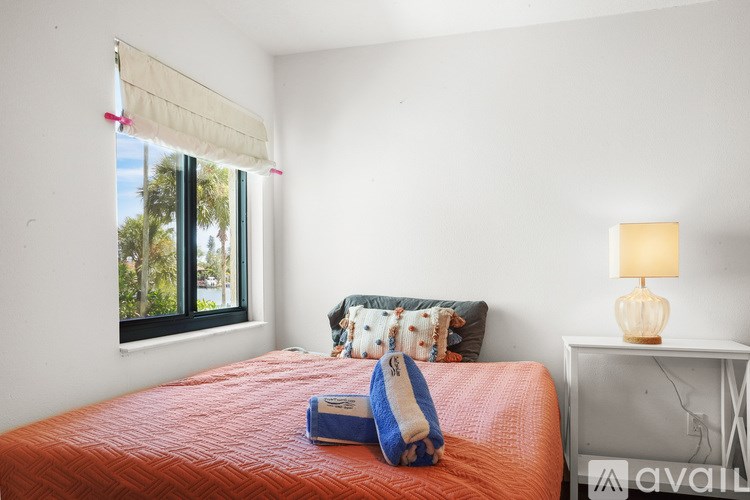 A bedroom with a red bedspread and a window with a view of trees.