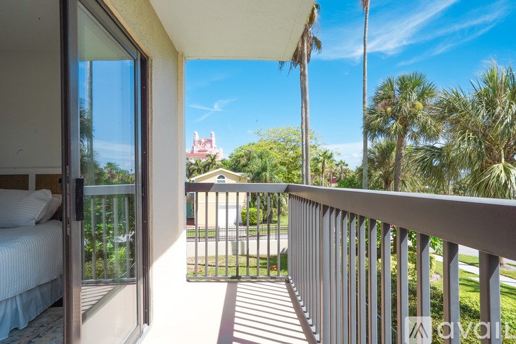 A balcony with a metal railing overlooks a park with palm trees and a building in the distance.