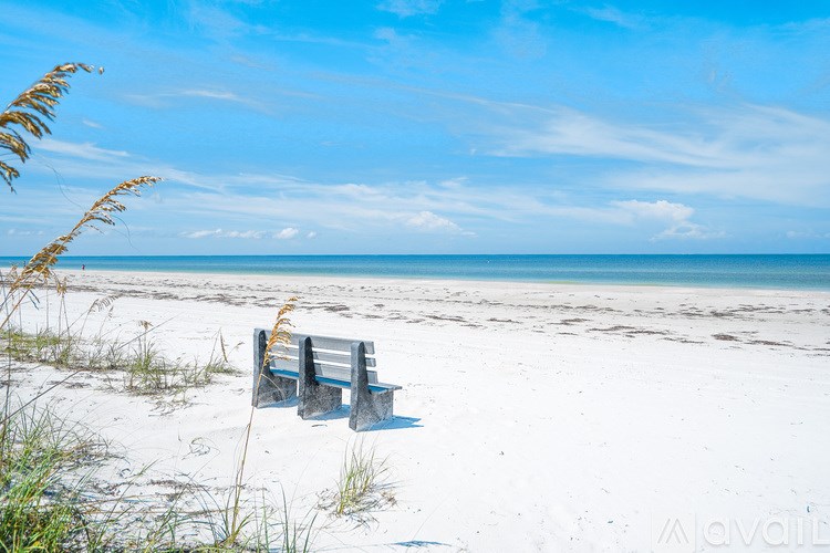 A beach scene with a blue sky and a single bench.