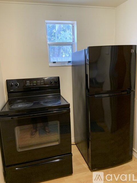 A black oven and refrigerator in a kitchen with a window.