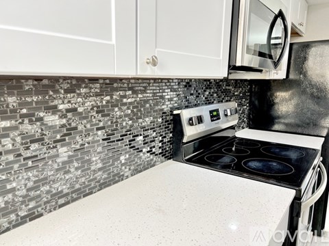 A kitchen with a black and white tile backsplash and a white stove top oven.